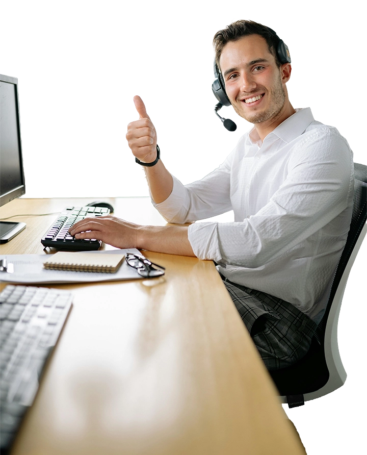 Smiling man wearing a headset, sitting in front of a keyboard and monitor, facing the camera