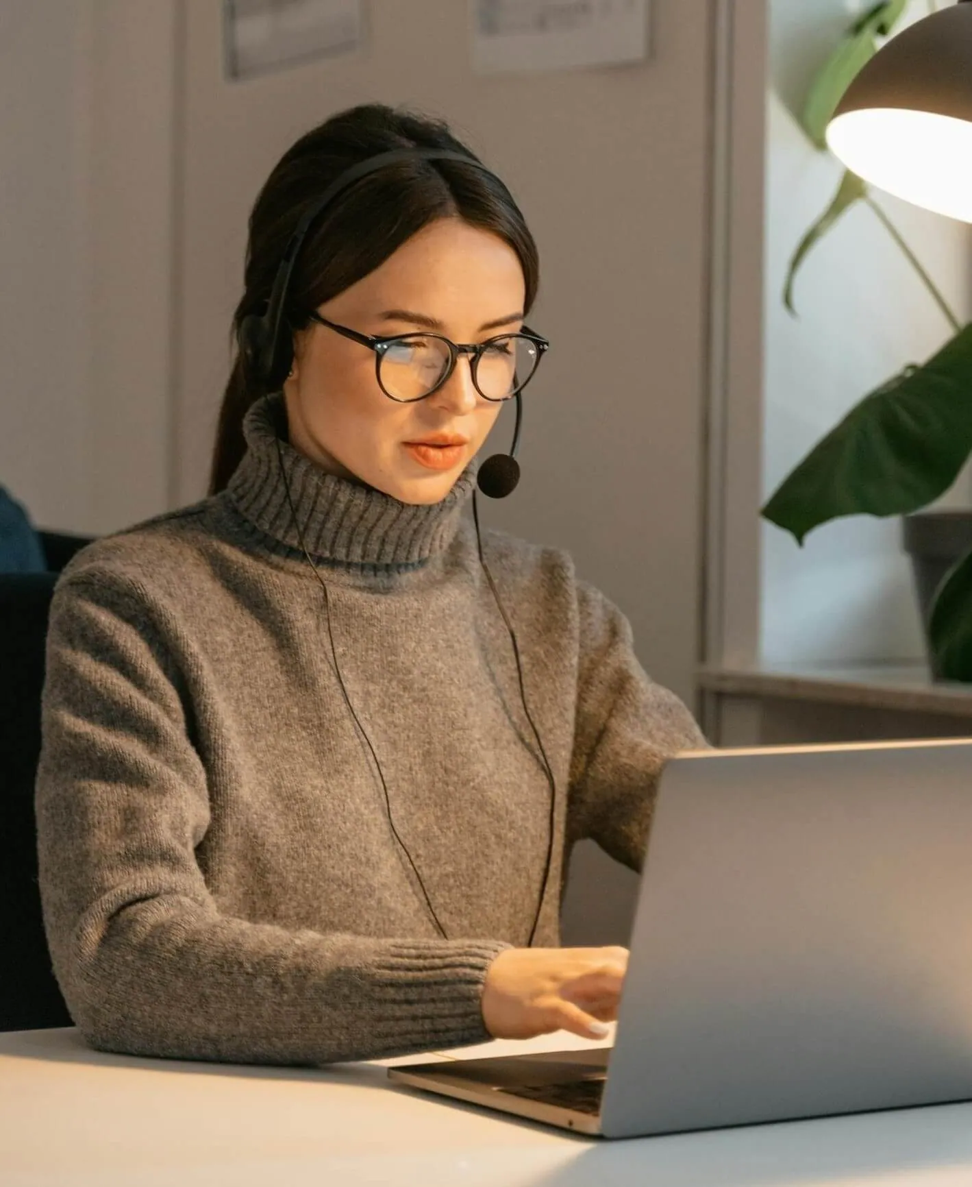 Woman talking on a headset while typing on a laptop